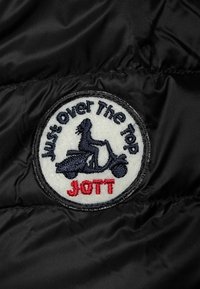 Rund broderad patch på svart tyg som visar en person som åker sparkcykel med texten "Just Over The Top" och "JOTT" i rött.