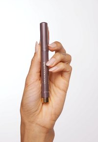 Brauner ausziehbarer Stift mit goldenem Akzent am Griff, der zwischen den Fingern gehalten wird. Glatte Textur, zylindrische Form und minimalistische Markenkennzeichnung.
