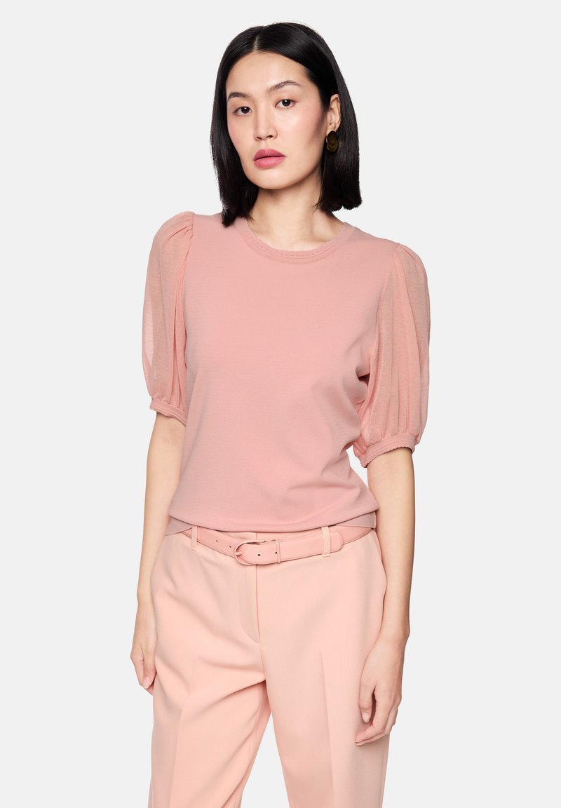 Light pink short-sleeve top with textured puff sleeves and a round neckline, paired with light pink belted trousers. Smooth fabric texture.
