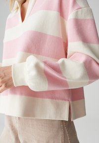 Roze-wit gestreepte pullover met kraag, met een losse pasvorm en geribde manchetten. Zachte gebreide textuur, met zijsplitten aan de zoom.