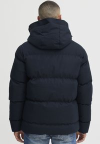 Mørkeblå pufferjakke med hætte, med quiltet design, tyk polstring og korte ærmer. Minimalistisk stil uden synlige logoer.
