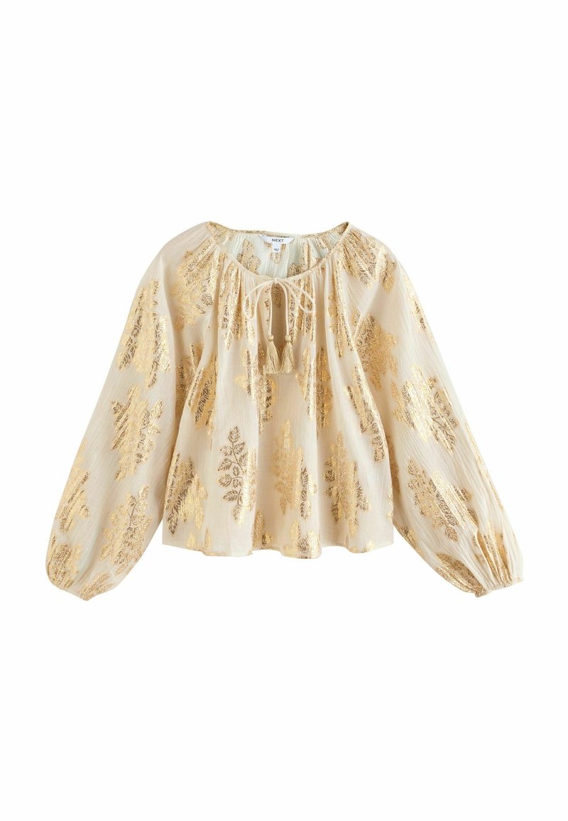 Blouse crème à manches longues avec motifs feuilles dorées, coupe ample, poignets froncés et lien à pompon au col rond.