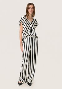 Set composto da blouse a righe bianche e nere e pantaloni a gamba larga, realizzato in tessuto leggero, con scollo a V e vestibilità rilassata, texture lucida, abbinato a tacchi neri a punta.