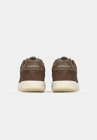 Brown suede athletic shoes with white accents and a textured cream sole; features a logo on the heel and padded collar for comfort.