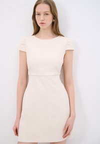 Knee-length, lyhythihainen mekko pehmeästä vaaleanbeigestä kankaasta. Ominaisuuksina pyöreä kaula-aukko ja hienovarainen laskostus olkapäissä lisäyksinä.
