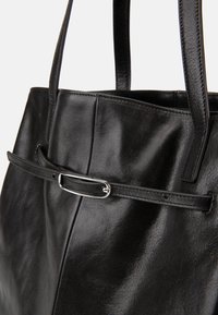 Črna usnjena torbica z dvema ročajema in tankim pasom, ki ima na sprednji strani majhno srebrno zaponko.