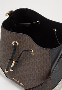 Borsa a secchiello marrone decorata con dettagli in pelle nera, hardware dorato e un interno morbido. Presenta chiusura a coulisse e dettaglio del logo.