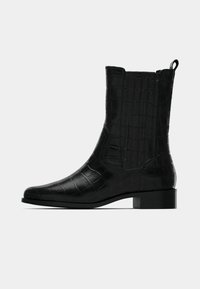 Crne gležnjače s teksturom krokodila, ravnim potplatom, zaobljenim vrhom i diskretnim bočnim rezovima za lakše obuvanje.