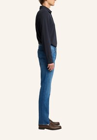 Polo shirt a maniche lunghe scuro abbinato a jeans in denim blu. I jeans presentano tasche posteriori e una vestibilità diritta, abbinati a mocassini marroni.