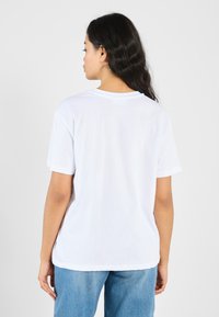 Hvid bomulds t-shirt med korte ærmer og rund hals, vist fra ryggen. Glat tekstur, løst fit og uden synlige mønstre.