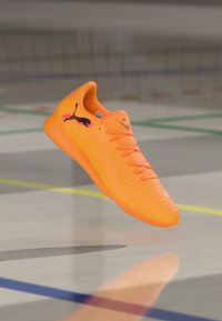 Puma footwear in vibrant orange with textured surface, prominent black logo, and traditional lacing system. Lightweight design for agility.
