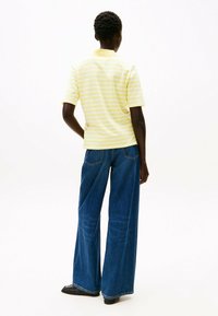 Camisa polo de manga corta a rayas amarillas combinada con jeans de mezclilla azules de corte holgado. Zapatos negros de punta afilada complementan el conjunto.