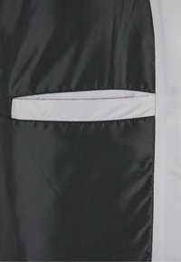 Un material textil negru cu o textură netedă prezintă o buzunar alb orizontal ca accent. Cusăturile sunt neat lucrate de-a lungul marginilor.