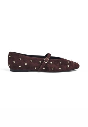 Chaussure plate Mary Jane en daim marron foncé avec des clous ronds dorés et une petite bride à boucle, vue latérale sur fond blanc.