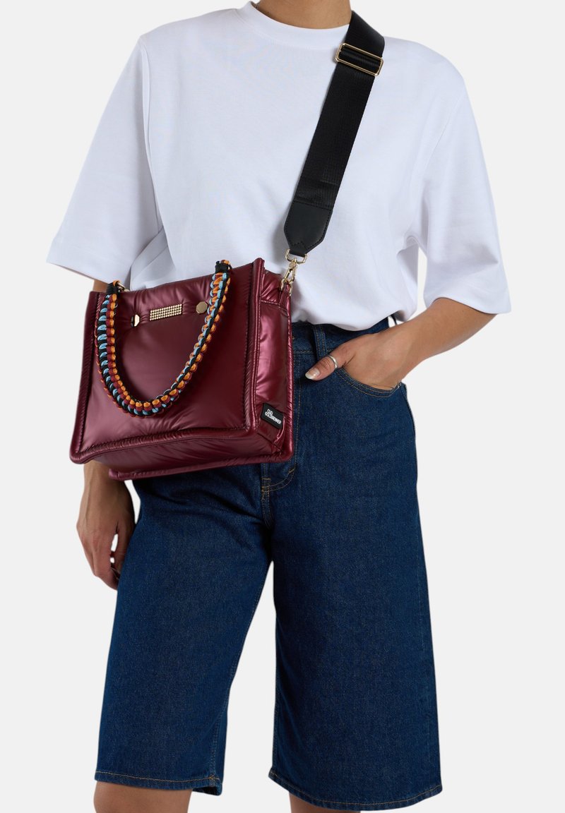 Bordeaux nylontas met een gevlochten, meerkleurige handgreep, voorzien van zilverkleurige hardware en een afneembare zwarte schouderband, gedragen crossbody.