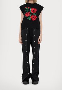 Czarny dzianinowy top z czerwonym kwiatowym haftem, zestawiony z czarnymi, wysokim stanem spodniami dżinsowymi z srebrnymi zatrzaskami po bokach.