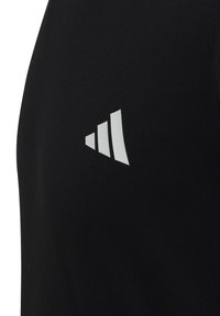 Camiseta atlética negra con un logo blanco que presenta tres barras ascendentes en el lado izquierdo del pecho. El material parece suave y elástico.