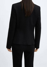 Blazer noir ajusté à manches longues et design structuré. Tissu uni, texture lisse, avec une fente simple à l'arrière.