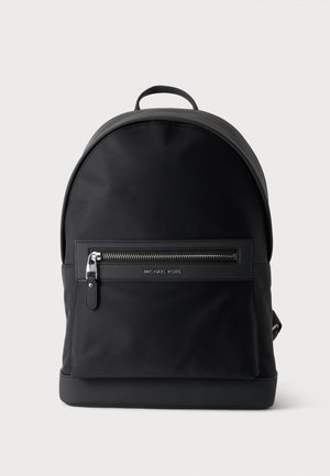 Schwarzer Michael Kors Rucksack mit einer vorderen Reißverschlusstasche und einem oberen Griff auf einem schlichten hellen Hintergrund.