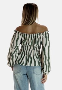 Blusa off-the-shoulder in tessuto crema con motivi a onde verdi, dotata di una vita arricciata e maniche lunghe e voluminose.