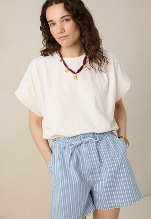 Chemise blanche à manches courtes, shorts rayés bleus et blancs avec une taille à cordon, et un collier pendentif bordeaux avec des accents dorés.