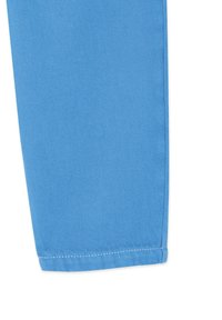 Gros plan d'une jambe de pantalon en denim bleu clair montrant une texture de tissage en diagonale et un ourlet cousu en bas.