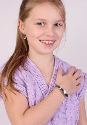 Zilveren hoefijzerhanger necklace, bijpassende oorbellen en een zwarte armband bij een meisje met een lavendel brei-top, die glimlacht, met licht haar.