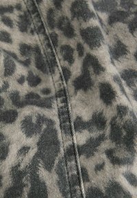 Leren stof met luipaardprint in grijstinten en zwart, met een zachte textuur. Zichtbare stiksels langs de naad voegen detail toe.