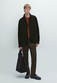 Mørkegrøn kordfløjlsskjorte, rustfarvet sweater, brune bukser, sorte sko og en mørk taske. Glatte overflader og knapdetaljer er synlige.