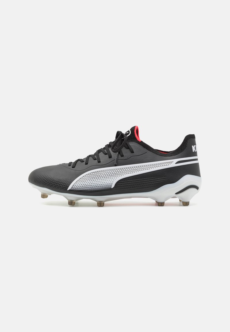 Botín de fútbol negro con textura sintética, con un acento plateado, cordones negros y detalles rojos en el talón y la lengüeta.
