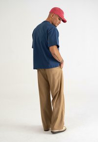 Marineblå oversized T-shirt med korte ærmer, sat sammen med khaki vide bukser. Modellen bærer en pink cap og har synlige tatoveringer.