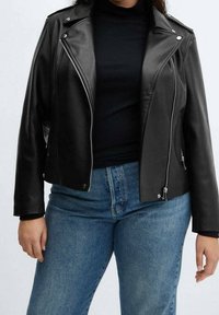 Femme portant une veste en cuir noire sur un haut noir associée à un jean bleu, vue du cou aux hanches sur un fond uni.