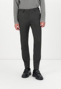 Graue taperte Hosen aus einem glatten, strukturierten Stoff mit einem einzigen Knopfverschluss, kombiniert mit schwarzen Slippern.