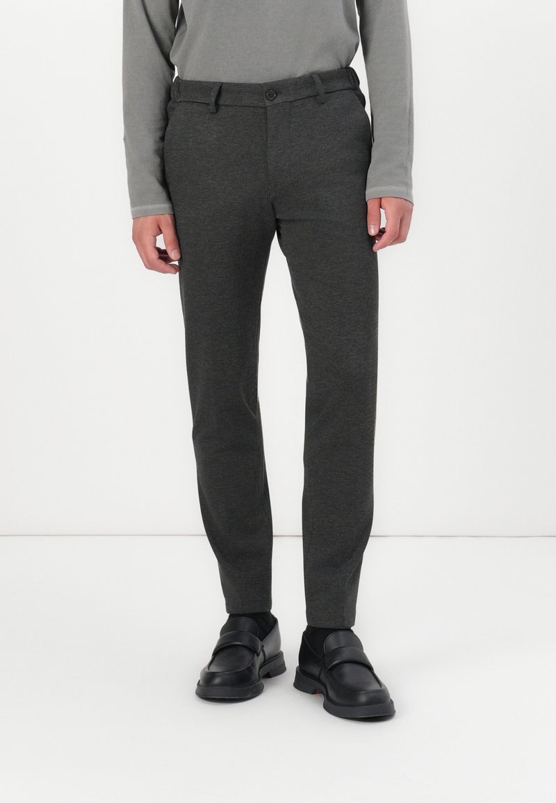 Graue taperte Hosen aus einem glatten, strukturierten Stoff mit einem einzigen Knopfverschluss, kombiniert mit schwarzen Slippern.