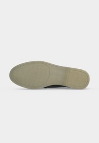 Semelle d'une chaussure habillée beige avec des motifs de grip texturés au niveau du talon et des orteils, présentée sur un fond clair uni.