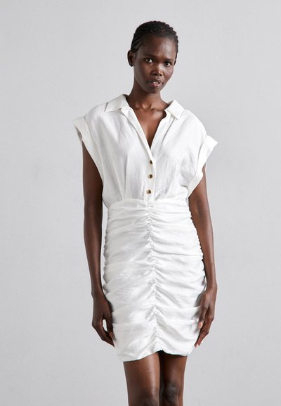 White linen dress with short sleeves, button-up front, and ruched detailing on the skirt for texture. Straight hemline with soft draping.