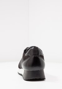 Svart sportskor med en blandning av glansigt syntetmaterial och matt mocka, med rundad häl och texturerad sula.