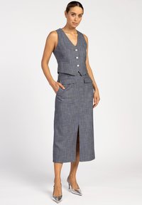 Mouwloos, grijs geruit jurkje met een V-hals, voorzakken, een gelaagd ontwerp en een kniehoog scheurtje. Gecombineerd met metallic hakken.