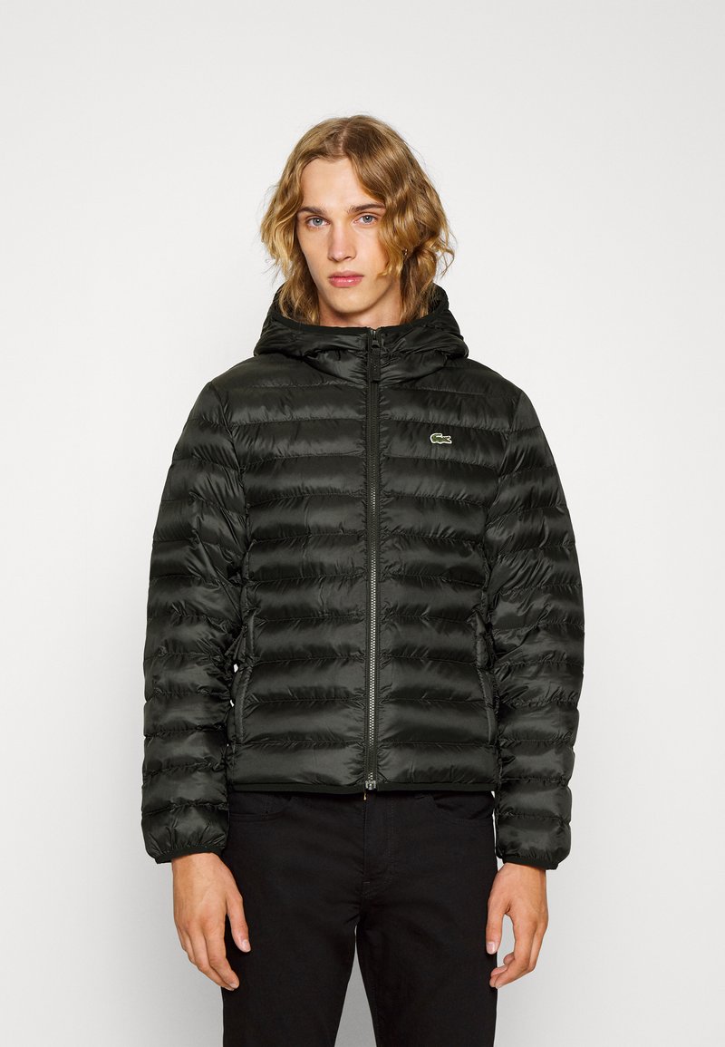 Schwarze, aufgeblasene Jacke mit Kapuze, mit horizontaler Steppung, einem Reißverschluss vorne und einem kleinen grünen Logo auf der linken Brust.