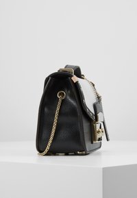 Borsa a mano in pelle nera con pannello bianco, finitura testurizzata, dettagli dorati e un accento a catena. Presenta un design elegante e strutturato.