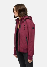 Bordeaux zip-up jakke med hette, med svart utstyr, snor, sidelommer og ribbede mansjetter. Glatt tekstur og tettsittende design.