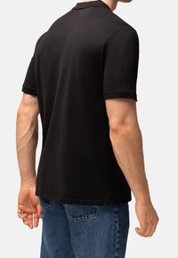 Svart polotröja i slät tyg, korta ärmar, med krage och sidslitsar. Buren med blå denimjeans.