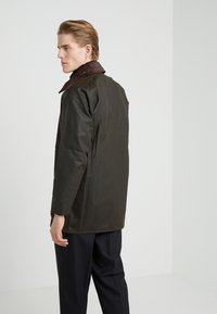 Brown corduroy-collared jacket in dark green material with a relaxed fit, shown from the back, featuring a simple design and no embellishments.