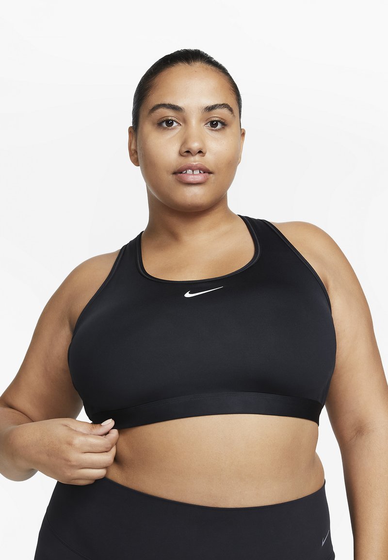 Sort sports-BH laget av elastisk materiale med bredt bånd og lite hvitt Nike-logo foran. Glatt tekstur og racerback-design.