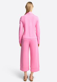 Completo in maglia rosa con giacca a maniche lunghe e pantaloni cropped a gamba larga. Tessuto liscio, vestibilità su misura e senza motivi visibili.