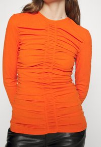 Långärmad topp i klargul tyg, med rynkad textur över framsidan och rund halsringning. Slät textur, smal passform.