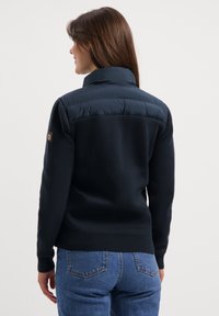 Marineblauwe fleece trui met gevoerde kraag en achterkant, geribbelde manchetten en zoom, met een logo patch op de mouw. Casual pasvorm en gestructureerde stof.