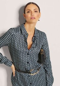 Navybluse mit weißem sechseckigem Muster, geknöpfter Front, Kragen, langen Ärmeln und einem schwarzen Gürtel mit einer goldenen runden Schnalle.