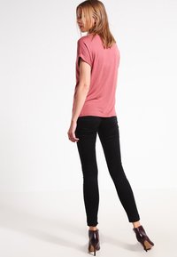 Rosa kortermet skjorte, avslappet passform, kombinert med svarte skinny jeans. Personen har på seg brune ankel støvler. Ensfarget bakgrunn.