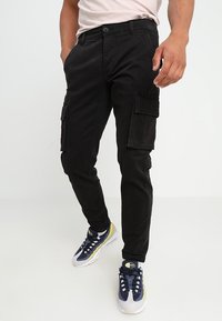 Czarna cargo ze slim fit, wykonana z bawełny, z wieloma bocznymi kieszeniami i klasycznym zapięciem na guzik. W zestawieniu z sportowymi trampkami.